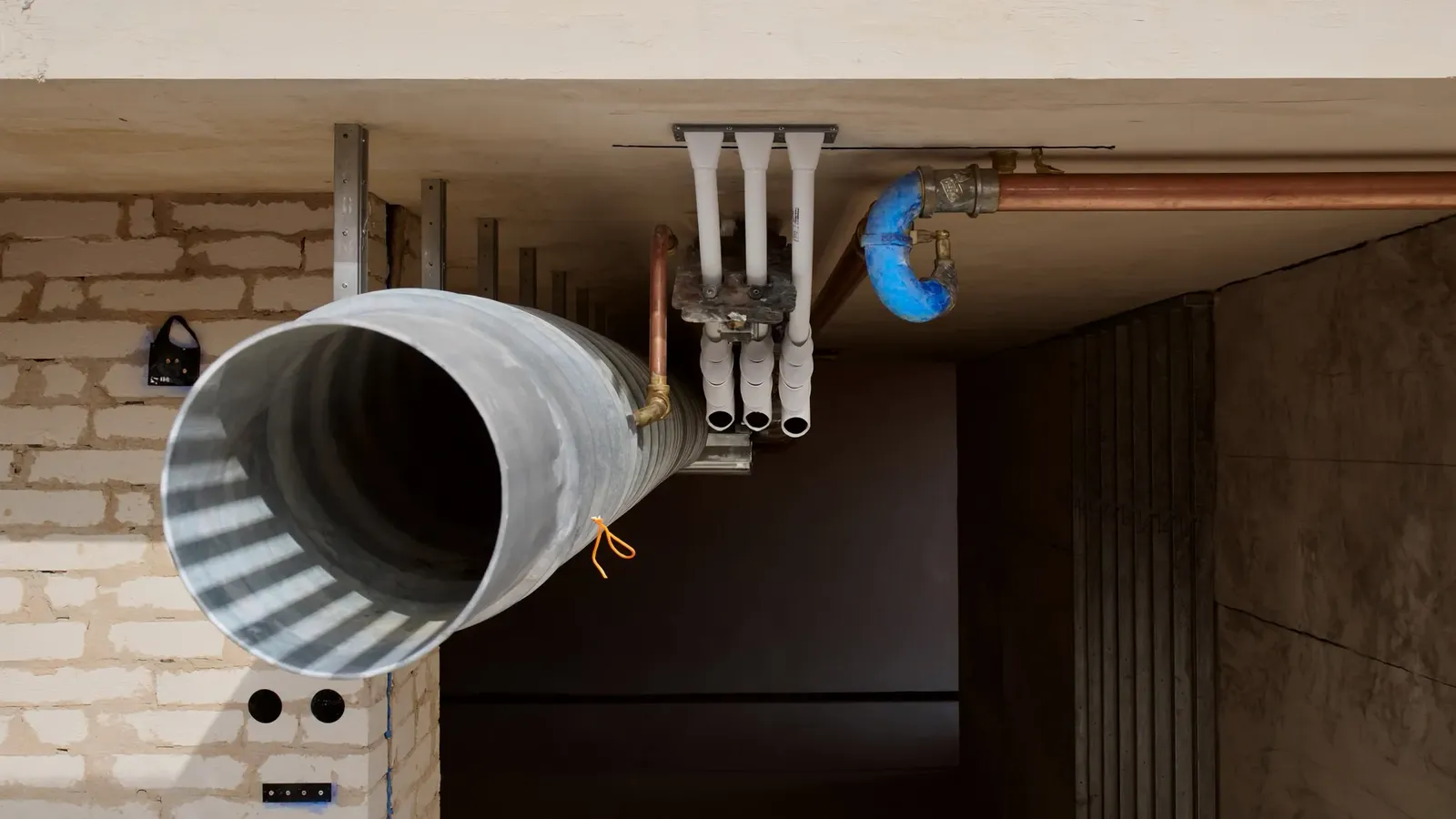 Spiral ductwork, dressed electrical conduit and copper pipework running in parallel through an open ceiling void before boarding