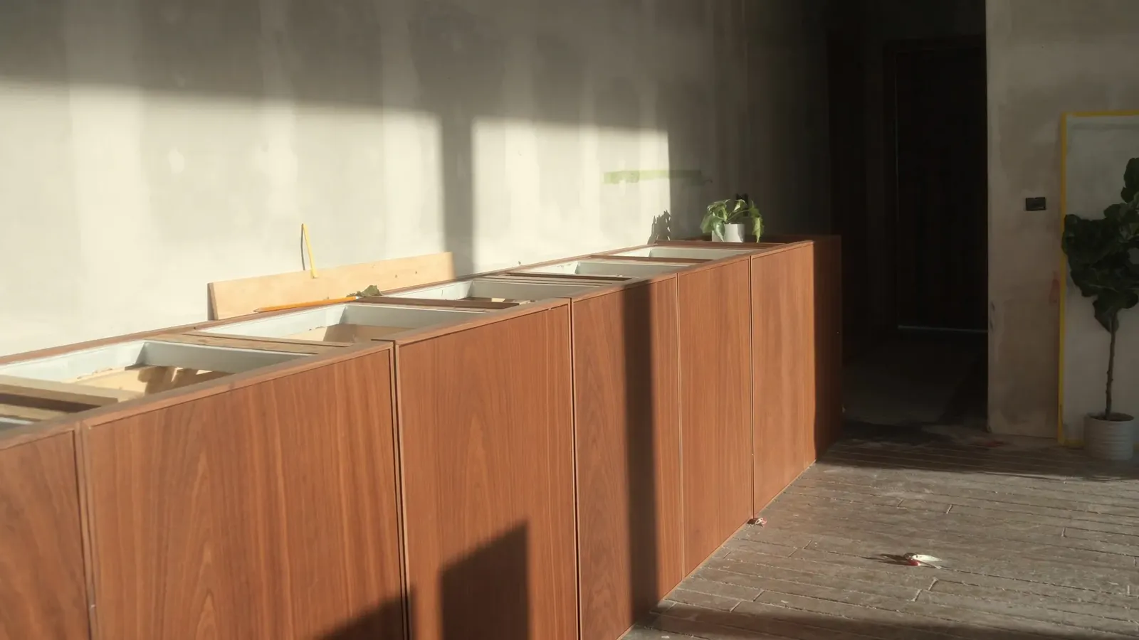 A fitted kitchen carcass at second fix, veneered joinery hung and set with even gaps, worktop not yet installed