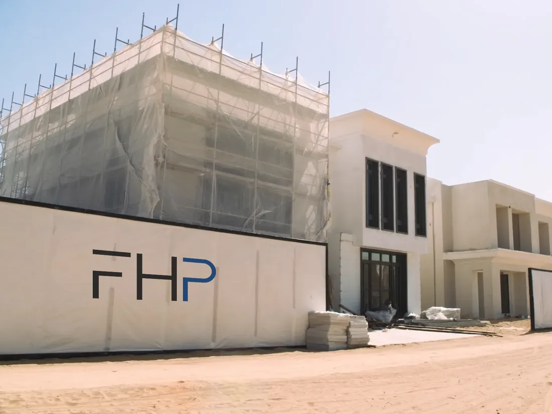 An existing villa under renovation, scaffold and netting on one wing and a site hoarding along the boundary