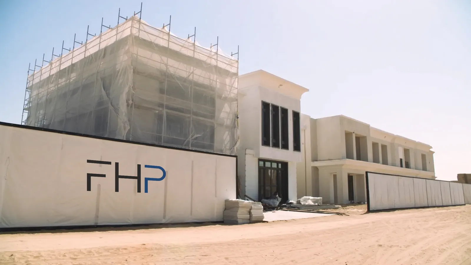 An existing villa under renovation: scaffold and netting on one facade, an FHP site hoarding along the boundary