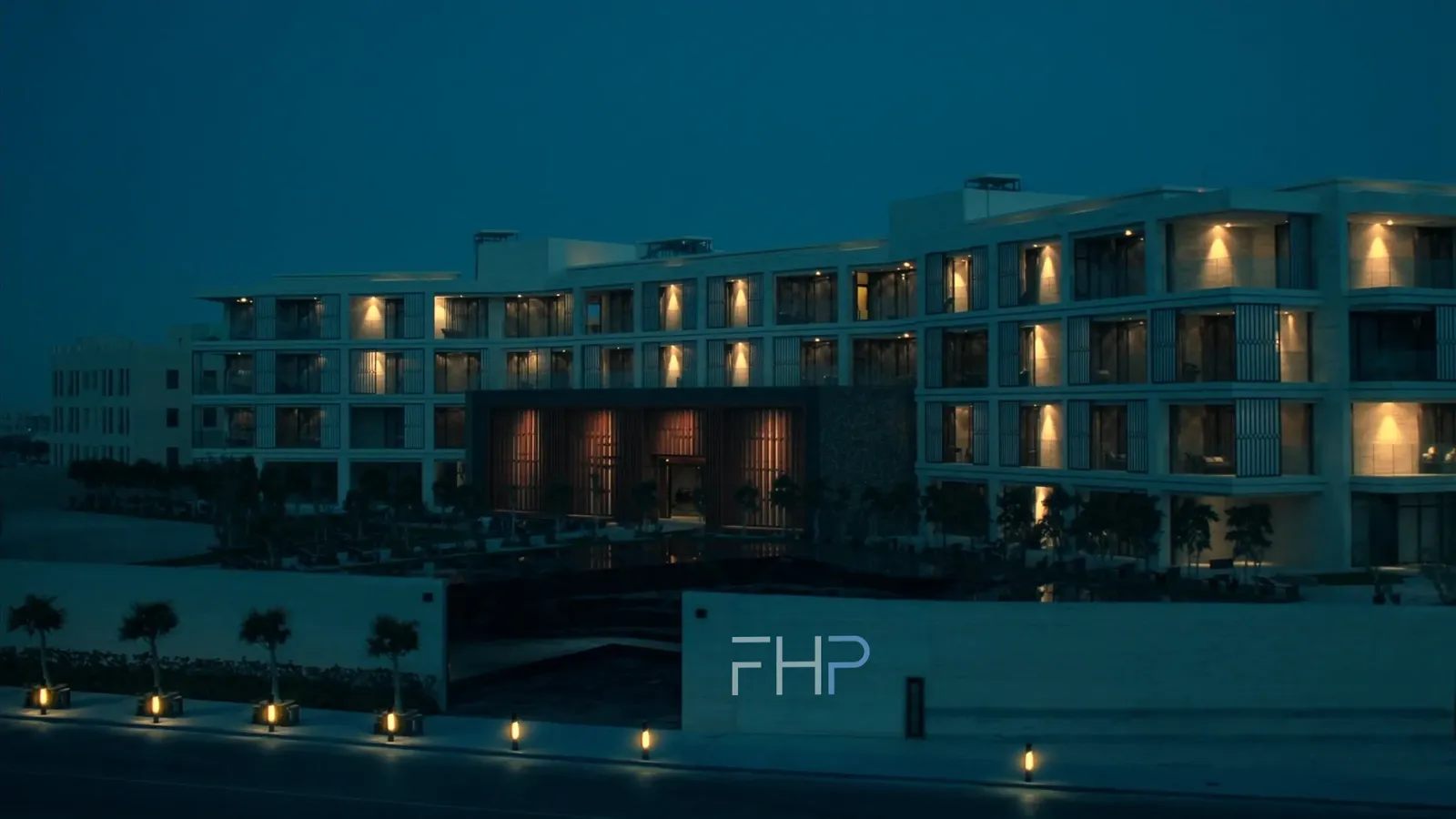 A completed five-storey residential building at blue hour, balconies lit, a reflecting pool in the forecourt