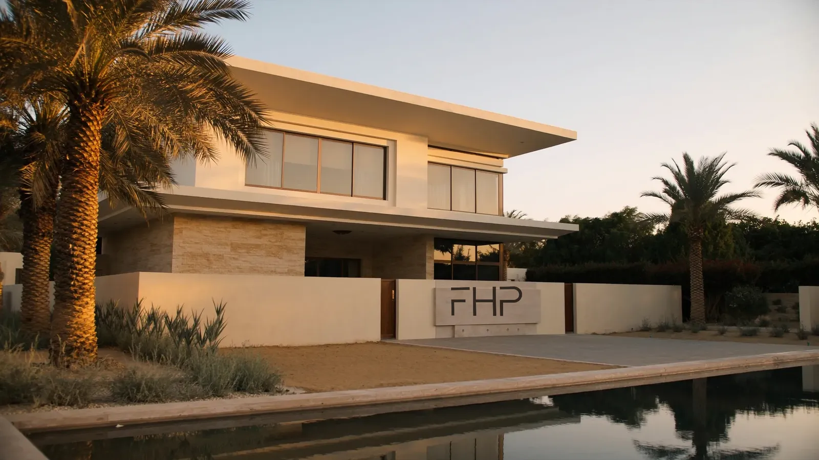 A finished villa at golden hour: limestone and render, palms, a pool, an FHP plaque on the boundary wall